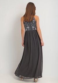 Schwarzes Maxikleid mit einem enganliegenden, mit Perlen besetzten Oberteil und einem fließenden, durchsichtigen Rock. Die Rückansicht zeigt verstellbare Träger und ein glattes Finish.