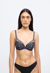 Μπλε σκούρο δαντελένιο σουτιέν με διάφανα πλέγματα στα πλάγια, διακοσμημένο με κεντήματα λουλουδιών και ρυθμιζόμενους ιμάντες, σχεδιασμένο σε τριγωνικό σχήμα.