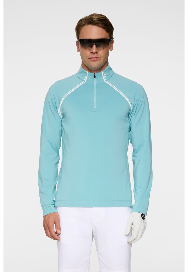 Ljusblå långärmad polo med kvartdragkedja, vit förstärkning längs sömmarna och vita handskar. Mjuk och atletisk tygtextur.