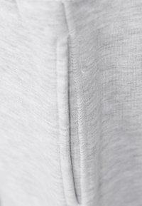 Jasnoszara tkanina o melanzowanym wzorze, z szwem biegnącym pionowo wzdłuż środka. Miękki, elastyczny materiał.