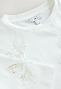T-shirt en coton blanc à col rond, ornée d'une broderie en sequins et perles représentant des papillons sur le devant.