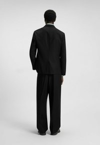 Black suit with a structured jacket and wide-legged trousers. Made of smooth fabric, features a vent at the back and cuff details on sleeves.