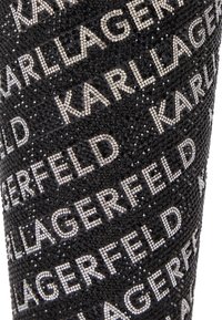 Tejido negro adornado con un patrón del nombre "KARL LAGERFELD" en cristales de zirconia plateados, con una superficie texturada y brillante.