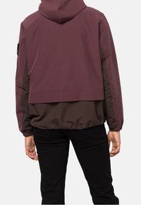 Veste à capuche bordeaux et marron au design court, avec des poignets élastiques et une texture lisse, ornée d'un patch logo sur le côté.