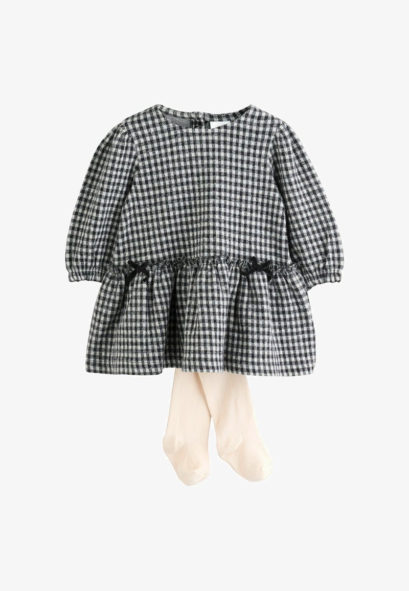Robe pour bébé à manches longues en noir et blanc à damier avec taille froncée et petits nœuds, accompagnée de collants de couleur crème.