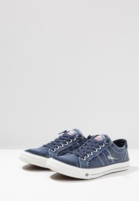 Canvas sneakers in navy blue with white rubber soles. Features include stitched accents, lace-up closure, and logo on the tongue.