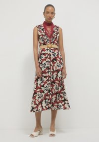 Floral midi dress in red, cream, and navy, featuring ruffled neckline, a belted waist with a circular accent, and a flowy silhouette.