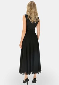 Czarna sukienka bez rękawów z dopasowanym gorsetem i zwiewnym, plisowanym dołem. Noszona z czarnymi szpilkami, które mają przezroczysty brzeg.