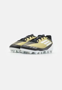 Scarpe da calcio nere e dorate con tre righe bianche, design aerodinamico, tomaia testurizzata e una suola bianca durevole con tacchetti.