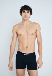 Boxers noirs avec un logo « BOSS » blanc sur la ceinture, design ajusté, texture lisse et longueur mi-thigh.