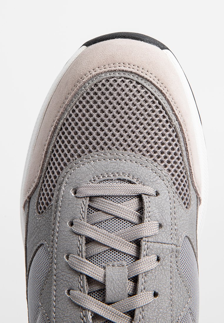 Graue Turnschuhe mit einem Obermaterial aus Mesh, Wildlederakzenten und flachen Schnürsenkeln. Sie verfügen über eine abgerundete Zehenpartie und eine strukturierten Gummisohle.