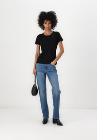 T-shirt nera a maniche corte con cuciture decorative al colletto, abbinata a jeans a gamba dritta blu chiaro e stivali neri a punta.