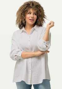 Witte blouse van textuurstof, met opgerolde lange mouwen, voorzien van knopen en een afgeronde zoom. Gecombineerd met denim jeans.