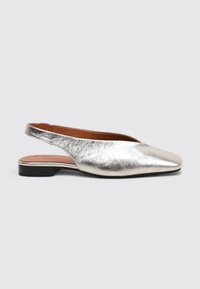 Zapato plano de piel plateada con tira trasera, punta afilada, tacón bajo negro y acabado texturizado. El interior cuenta con una plantilla en tono marrón.