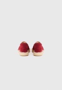 Crvene suede espadrile s okruglim oblikom i prirodnim jutenim potplatom, s tkanim detaljima na rubu. Minimalistički dizajn, bez ukrasa.