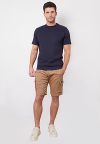 Námorníci s krátkým rukávem v námořnické modři, spárované s khaki cargo šortkami s bočními kapsami, nošeno se světle barevnými teniskami.
