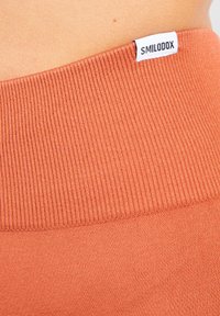Oranje geribde tailleband met een witte merklabel met de tekst "SMILODOX." De textuur is glad en elastisch, ontworpen voor comfort.