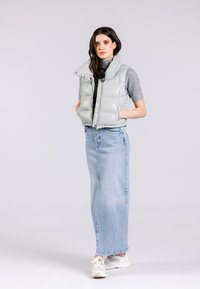 Gilet morbido grigio chiaro con colletto alto e zip, indossato sopra un top grigio e una gonna maxi in denim, abbinato a sneakers bianche.