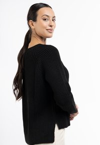 Pulover tricotat negru cu textură ribbed, decolteu rotund și slituri laterale. Mâneci lungi cu manșete ajustate, conceput pentru o croială relaxată.