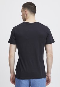 Svart bomull t-skjorte med rund hals og korte ermer, med et enkelt design og en glatt tekstur, vist fra baksiden.