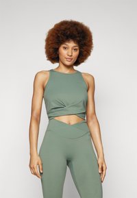 Olivenfarget sports crop top med vridd frontdesign, matchende høyhullet leggings, begge laget av glatt, elastisk stoff.