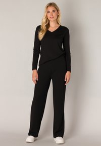 Black long-sleeve V-neck top paired with loose black pants. Smooth fabric with a soft texture, complemented by white sneakers.