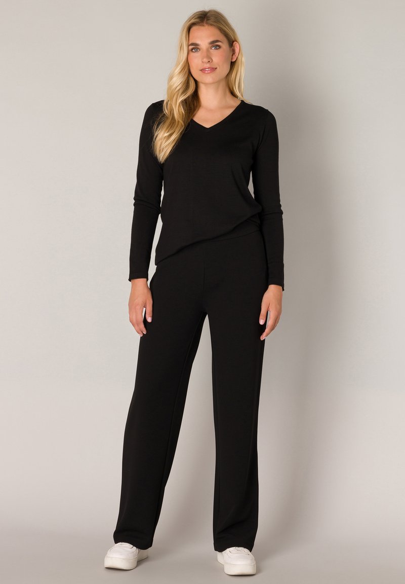 Black long-sleeve V-neck top paired with loose black pants. Smooth fabric with a soft texture, complemented by white sneakers.