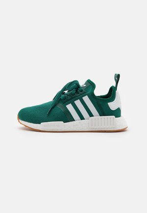 Baskets Adidas vert foncé avec bandes blanches, semelle blanche, semelle extérieure en gomme et boucle au talon sur fond blanc, vue de côté.
