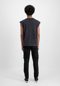 Top din bumbac negru fără mâneci, spălat cu piatră, cu margini brut, asortat cu pantaloni cargo negri tapered, având buzunare laterale mari și manșete elastice.