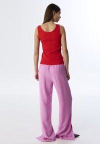 Czerwona prążkowana koszulka bez rękawów oraz miękkie różowe spodnie o szerokich nogawkach. Strój wyróżnia się dopasowanym fasonem, okrągłym dekoltem oraz bocznymi rozcięciami na spodniach.