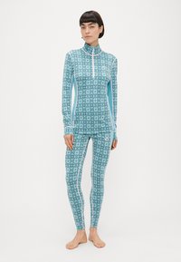 Τυρκουάζ σετ θερμικής ένδυσης με ψηλό γιακά, φερμουάρ στο στήθος και γεωμετρικό μοτίβο. Κατασκευασμένο από ελαστικό, μαλακό ύφασμα με αντίθετες γαλάζιες λεπτομέρειες.