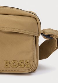 Τσαντάκι ώμου από ταμπά ύφασμα με φερμουάρ, ρυθμιζόμενο λουρί και ανάγλυφο λογότυπο "BOSS" στο μπροστινό μέρος. Λεπτομέρεια με υφή στην επιφάνεια.