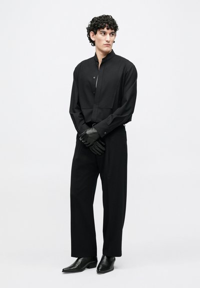 Melna garām piedurknēm krekls ar augstu apkakli, pieguļoša piegriezuma un priekšpuses pogu aizdare. Kombinēts ar melnām biksēm un ādas cimdiem.