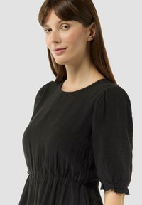 Schwarzes Kleid aus leichtem, strukturiertem Stoff. Verfügt über einen runden Ausschnitt, kurze Puffärmel und eine taillierte Taille mit einem ausgestellt Rock.