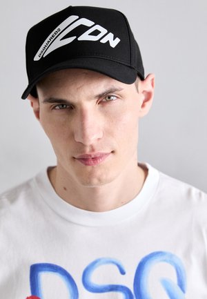 Casquette noire avec logo blanc "DSQUARED2" et "ICON" à l'avant. T-shirt blanc avec un design de texte coloré. Esthétique simple et moderne.