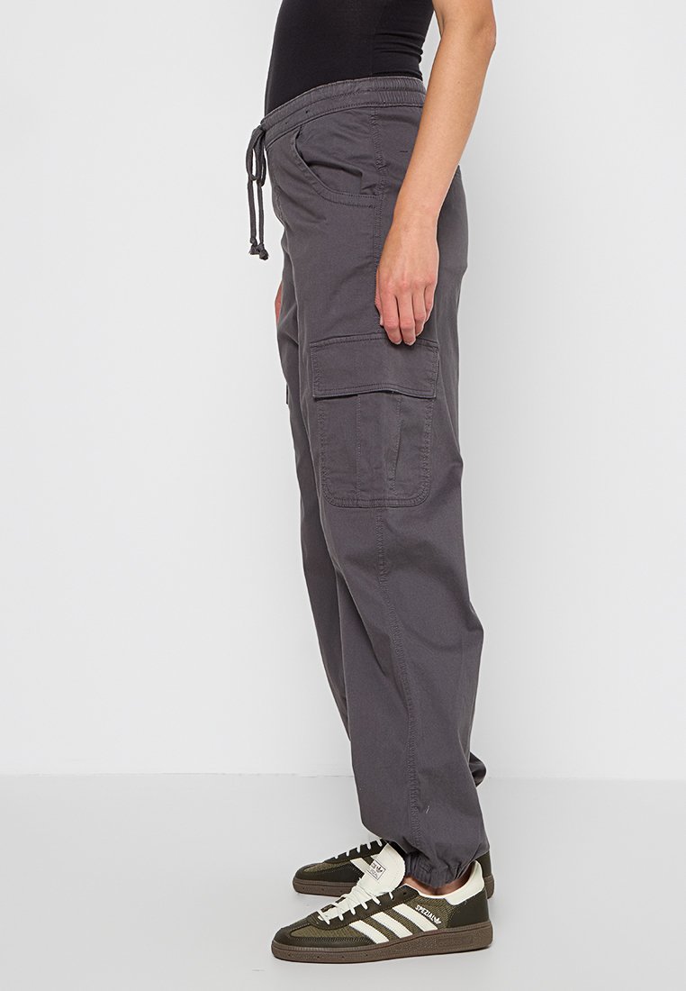 Szare spodnie cargo z elastycznym paskiem w talii, kieszeniami bocznymi i luźnym krojem, wykonane z lekkiego materiału. Ozdobione detalami przeszyć.