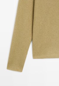 Beige gestrickter Pullover mit langen Ärmeln, Ärmel und Seite auf weißem Hintergrund gezeigt, wobei die Textur und das Stoffdetail hervorgehoben werden.
