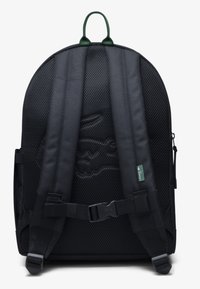 Schwarzer Rucksack mit Mesh-Stoff, gepolsterten Trägern und einem grünen oberen Tragegriff. Verfügt über ein tonales Logo-Design und verstellbare Schnallen.