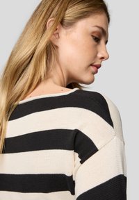 Strickpullover mit horizontalen schwarzen und cremefarbenen Streifen. Leicht slouchy Schultern mit strukturiertem Stoff und entspanntem Schnitt.