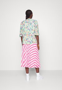 Blouse à manches courtes à motif floral aux tons verts, bleus et orange, associée à une jupe plissée à rayures roses et blanches et des baskets blanches.