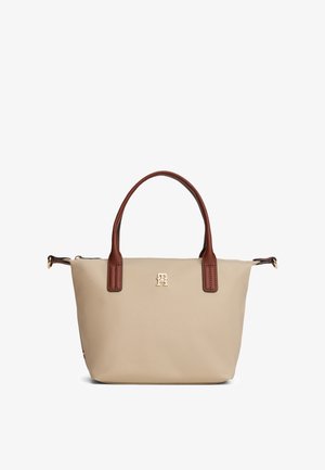 Beige handlenett med brune håndtak, lite gyllent logo midtstilt under håndtakene, og glidelåslukking på toppen.