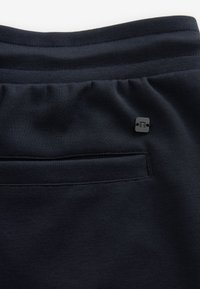 Pantalons de jogging bleu marine avec un tissu texturé. Présente un design fuselé, une taille élastique et un petit logo noir près de la poche.