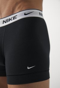 Boxers negros de Nike con una amplia cinturilla blanca que presenta el nombre de la marca. Incluye un pequeño logo blanco en el lado inferior izquierdo.