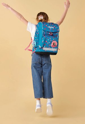 Blue backpack with pink polka dots, two front pockets, adjustable straps, and bicycle graphic detail. Flat base for stability.
