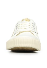 Sneaker bianca in tela con suola in gomma testurizzata, sei occhielli metallici e logo dorato sulla linguetta, caratterizzata da un classico design con lacci.