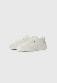 Un paio di sneaker bianche basse con lacci, lati testurizzati e suole bianche spesse su sfondo bianco uniforme.