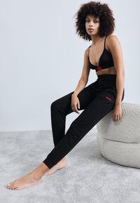 Black athletic bra with a red logo, paired with black sweatpants featuring a matching logo, both made from soft, comfortable fabric.
