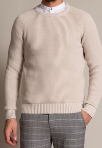 Pullover a maglia color beige chiaro con texture a costine, scollatura rotonda e maniche lunghe, abbinato a pantaloni a quadri grigio con motivo.
