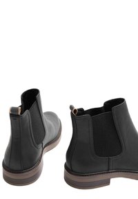 Botas de tobillo de cuero negro con un acabado suave, paneles elásticos en los laterales y una suela marrón contrastante con costuras decorativas.