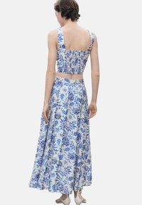 Zweiteiliges Outfit mit einem kurzessigen Oberteil mit quadratischem Ausschnitt und einem langem Rock mit floralem Muster in Blau- und Weißtönen.